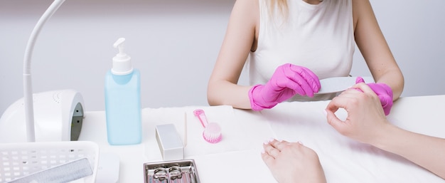 Manicurist does manicure with nail file. Professional workplace, small business, spa procedure, beauty industry concept