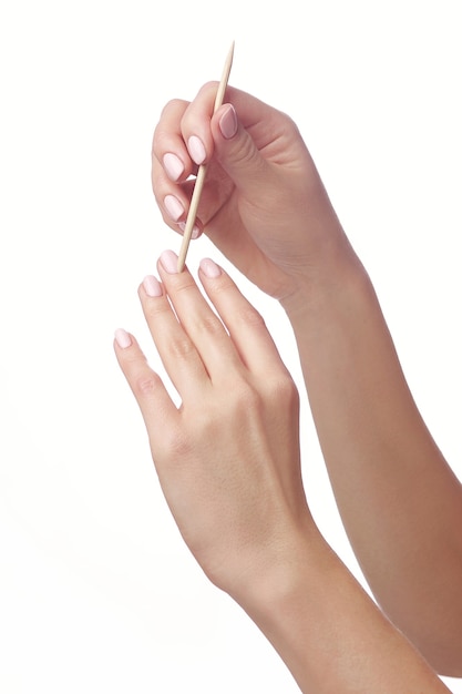 Manicurist doing cleaning cuticle on the female fingers with cosmetic stick