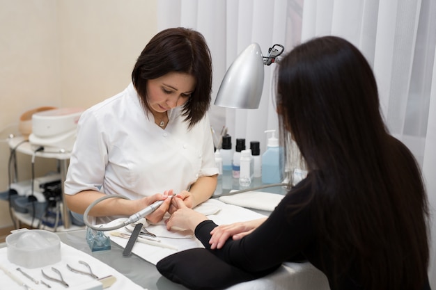 Manicurist doing hardware manicure to a young beautiful girl in the spa salon