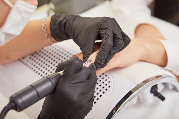 Manicurist doing manicure for client with electric nail machine