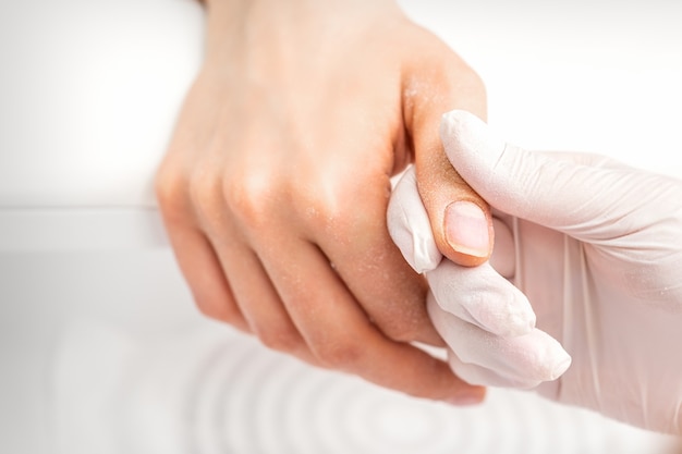 The manicurist holds the woman's thumb during a manicure procedure in the nail salon