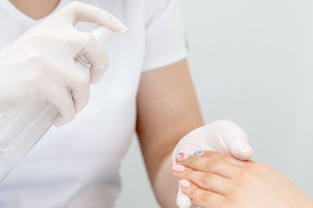 Manicurist is appies spray on client hand.