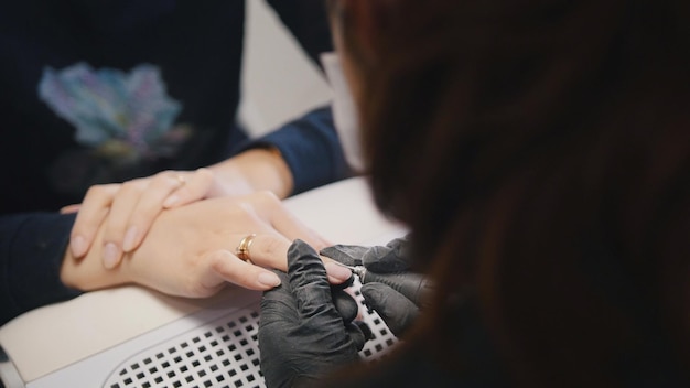 Manicurist in medical mask doing manicure for attractive woman in beauty salon, horizontal