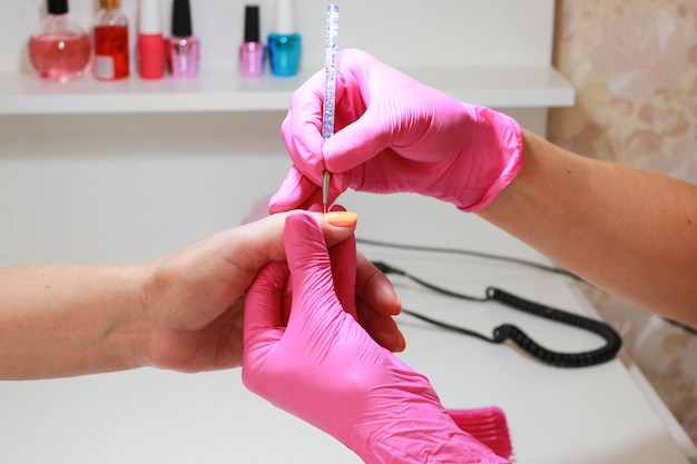 Manicurist in pink gloves makes a manicure applies orange nail polish with a thin brush