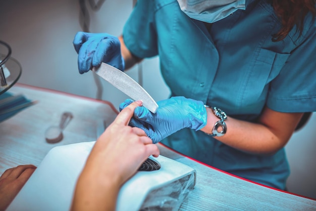 Manicure che rimuove la cuticola dall'unghia del cliente della ragazza al salone di bellezza.