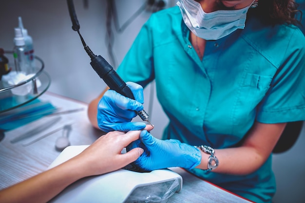 Manicurist removing cuticle from the girl client nail at beauty salon.