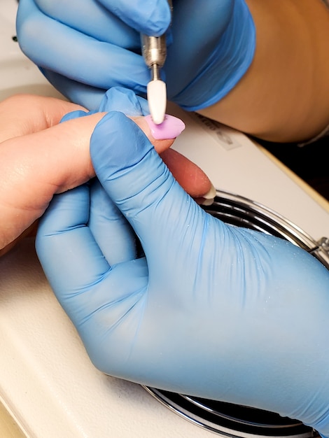 Manicurist uses an electric nail file drill for manicure on women's fingers