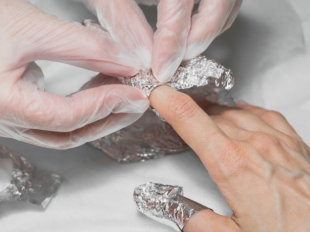 Manicurist wrapping finger nails with foil during the procedure of manicure at a Spa salon. Close up.