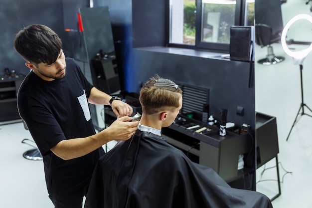 Mannelijk kapsel met elektrisch scheerapparaat. Kapper maakt kapsel voor klant bij de kapper met behulp van haarclipper. Man kappers met elektrisch scheerapparaat.