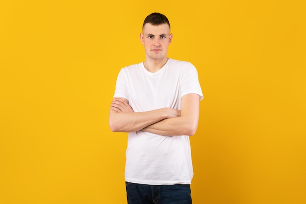 Mannelijk portret Knappe blanke man met gevouwen armen kijkend naar de camera met een t-shirt die zich voordeed op een gele achtergrond