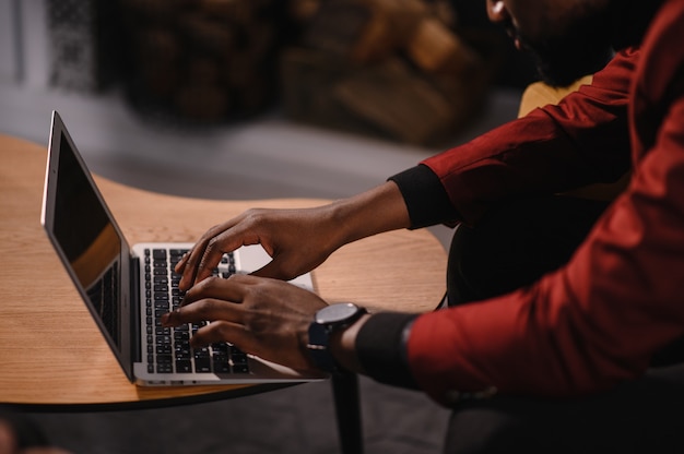 Mannelijke Afro-Amerikaanse gebruiker handen typen op laptop toetsenbord zitten aan tafel, student professionele studie werken met pc-softwaretechnologie concept, close-up.