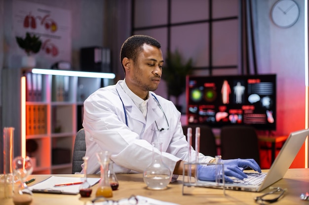 Mannelijke Afro-Amerikaanse wetenschapper testexperiment in science lab met behulp van laptopcomputer