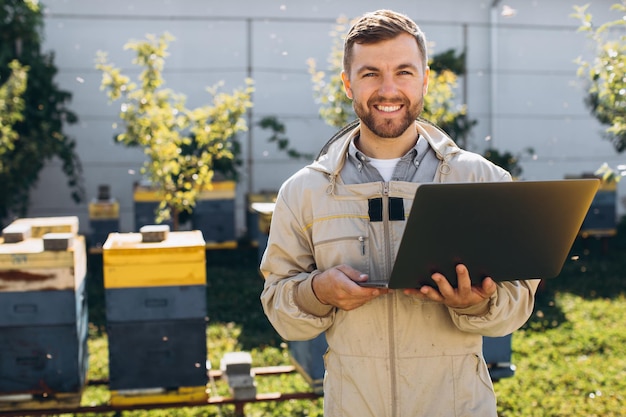 Mannelijke agronoom of ingenieur in beschermend pak die aan laptop bij bijenlandbouwbedrijf werkt