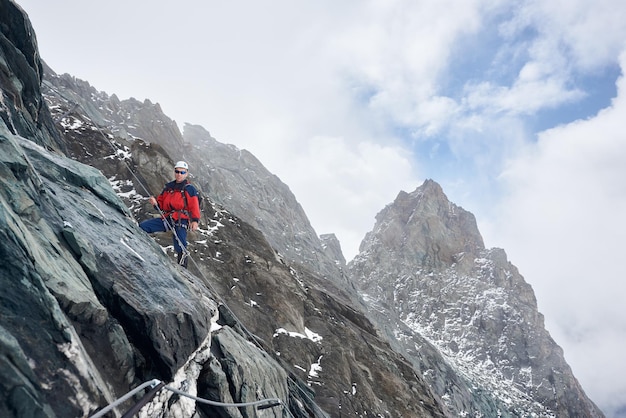 Mannelijke alpinist die hoge rotsachtige berg beklimt