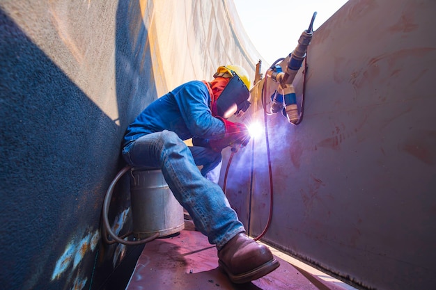 Mannelijke arbeider die beschermende kleding draagt en reparatielassen van industriële bouwolie en gas of opslagtank in besloten ruimten repareert.