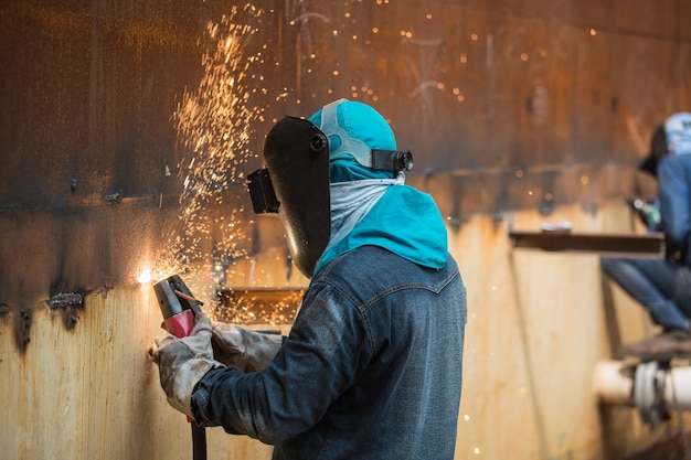 Mannelijke arbeider die beschermende kleding draagt en repareert lasvonkplaat industriële constructie olie- en gas- of opslagtank in besloten ruimtes.