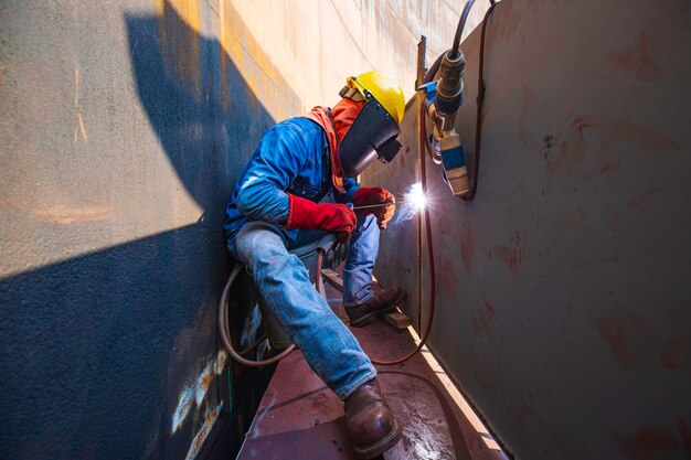 Mannelijke arbeider die beschermende kleding draagt en repareert laswerk voor industriële constructie olie en gas of opslagtank in besloten ruimtes