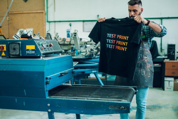 Mannelijke arbeider die een droogoven gebruikt voor t-shirt in een werkplaats