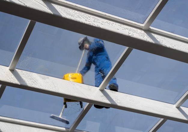 Mannelijke arbeider die grote uitgestrektheid van glasdak over zwembad wast