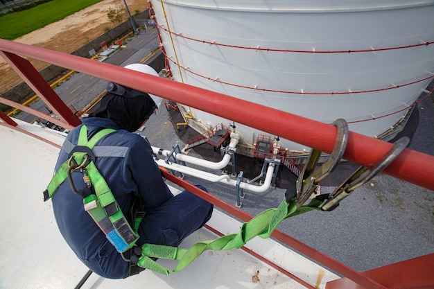 Mannelijke arbeider die veiligheidsharnas draagt en alleen werkt op een hoge leuning op open tankdakolie