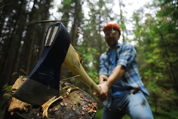 Mannelijke arbeider met een bijl die een boom in het bos hakt.