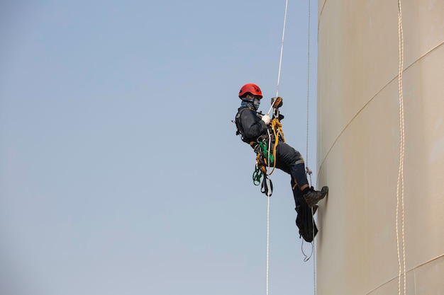 Mannelijke arbeider touw toegang industrieel werken op hoogte tank olie dragen harnas helm veiligheidsuitrusting touw toegang inspectie van dikte tank