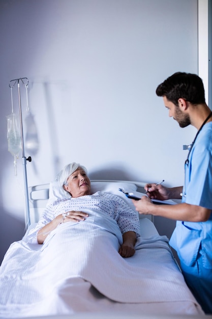 Mannelijke arts bespreekt medisch rapport met vrouwelijke senior patiënt op bed