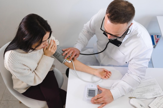 Mannelijke arts bij het medisch onderzoek meet de bloeddruk van een vrouwelijke patiënt. Vrouw op afspraak bij cardioloog