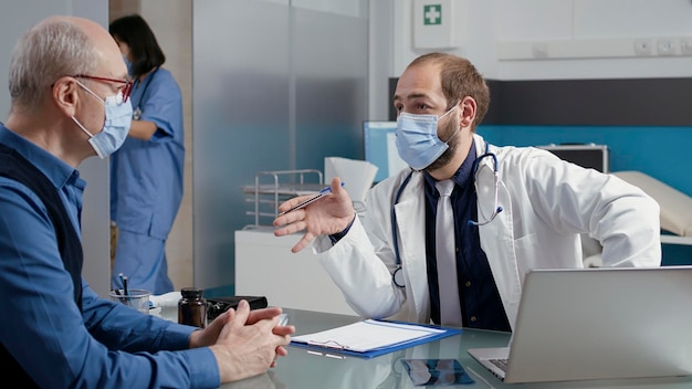 Mannelijke arts die aantekeningen maakt bij een consultatieafspraak met de oude man, die medicijnen op recept geeft om ziekte te genezen. specialist die controleonderzoek doet met gepensioneerde volwassene tijdens covid 19 pandemie.