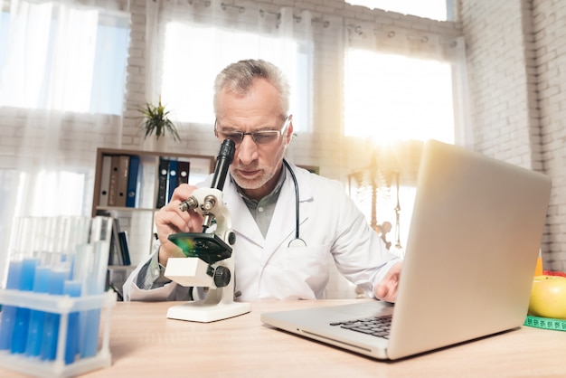 Mannelijke arts die door een microscoop in een laboratorium kijkt.