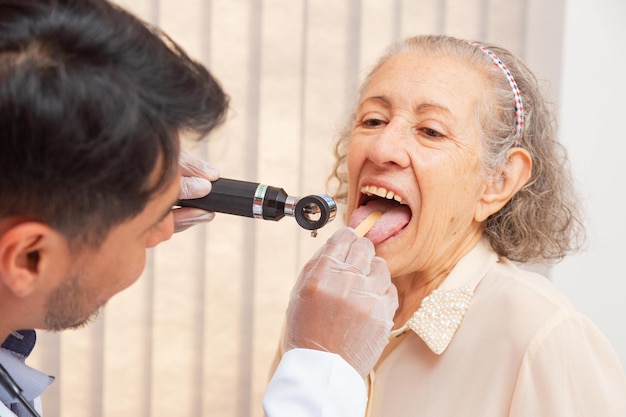 Mannelijke arts die in overleg de keel van een oudere vrouw onderzoekt. Dokter controleert keel oude vrouw