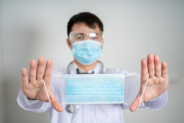 Mannelijke arts dragen PPE met een stethoscoop op schouder en trek stretch gezichtsmasker geïsoleerd op grijze achtergrond concept gezondheidszorg en medisch