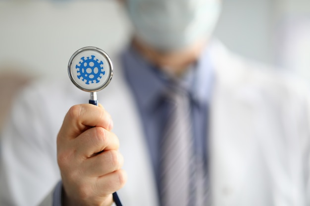 Mannelijke arts houden in de hand stethoscoop met coronavirus symbool close-up.