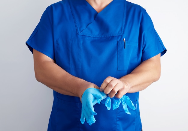 Mannelijke arts in blauwe uniform zet op zijn handen witte steriele latex handschoenen voor de operatie