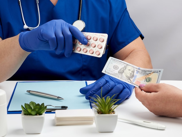 Mannelijke arts in uniform en in blauwe latex medische handschoenen zit aan een tafel en geeft een pakket pillen aan een patiënt