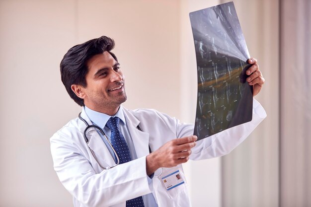 Mannelijke arts met een witte jas die in de ziekenhuisgang staat en naar CT- of MRI-scan kijkt