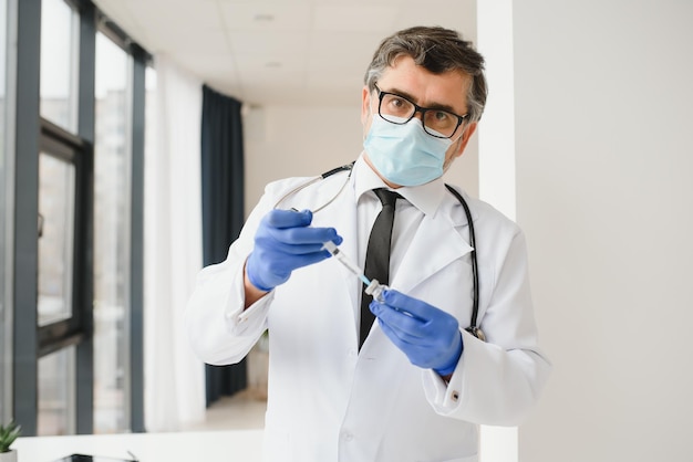 Mannelijke arts met uniform masker medische handschoenen met spuit die covid 19 corona-virusvaccin uit flaconfles neemt en zich voorbereidt op injectie Coronavirus immunisatie griepbehandeling vaccinatie