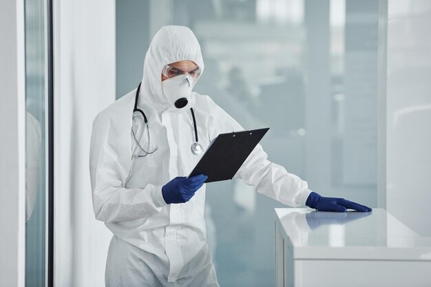 Mannelijke arts wetenschapper in laboratoriumjas defensieve brillen en masker met notitieblok in handen