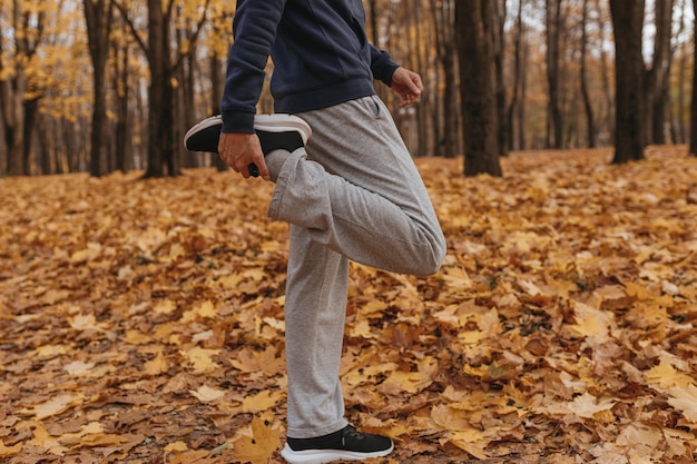mannelijke atleet in sportkleding die het been uitrekt terwijl hij in het herfstpark staat