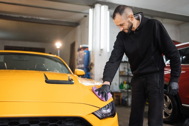 Mannelijke autowasserette houdt de microvezel in de hand en polijst de motorkap