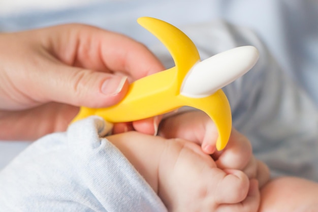 Mannelijke baby houdt bananenbijtring in zijn hand ontwikkeling en massage van het tandvlees close-up bijtring