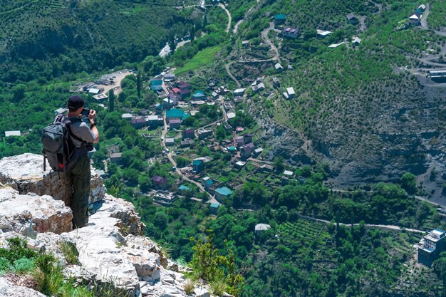 Mannelijke backpacker maakt foto's van een bergdorp vanaf een hoge klif