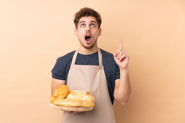 Mannelijke bakker die een lijst met verscheidene broden op beige houdt richtend met de wijsvinger een groot idee