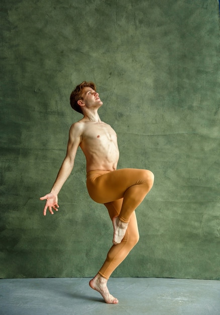 Foto mannelijke balletdanser poseert bij grunge muur in dansstudio. artiest met gespierd lichaam, gratie en elegantie van dans