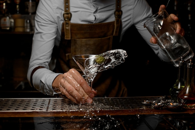 Foto mannelijke barman die een alcoholische drank in het martini-glas mengen met één olijf