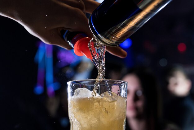 Mannelijke barman schenkt vakkundig een alcoholische cocktail in een glas