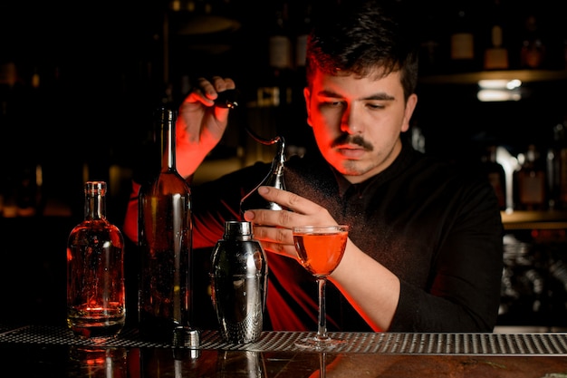 Mannelijke barman spuiten van de diffuser op de heerlijke cocktail in het glas