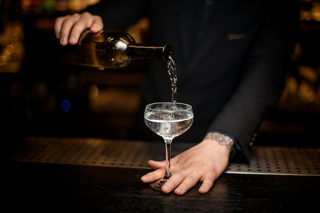 Mannelijke barman voegt champagne in een glas toe