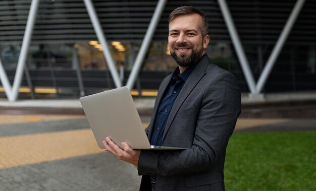 Mannelijke bedrijfsanalist met een laptop op de achtergrond van een kantoorgebouw