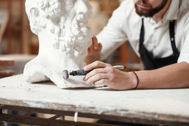 Mannelijke beeldhouwer repareert gipsbeeld van vrouwenhoofd op de werkplek in de creatieve